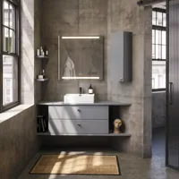 Badezimmer mit schrägen Wänden, grauem Waschtisch und Oberschrank, maßgefertigte Arbeitsplatten, modernes quadratisches Aufsatzwaschbecken, quadratischer Spiegel mit Beleuchtung, rohe Betonwände und -böden verleihen einen urbanen Ausdruck