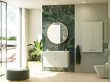 Stilvolles und luxuriöses Badezimmer mit sanften grünen Nuancen, einem großen eleganten runden Spiegel und einer modernen, raffinierten grünen Toilette