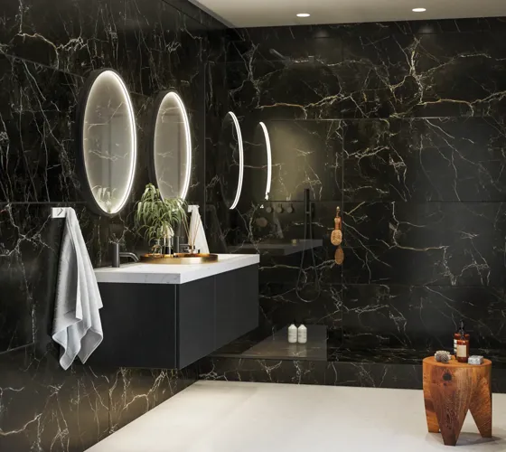 Elegante und moderne Badezimmer Inspiration mit dunklen Marmorwänden, runden beleuchteten Spiegeln mit schwarzem Rahmen, wandmontiertem Waschtischunterschrank mit Doppelwaschbecken und geräumiger Duschnische