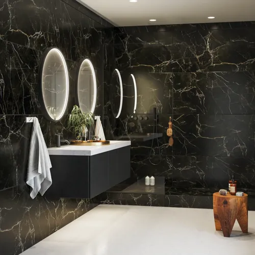 Elegante und moderne Badezimmer Inspiration mit dunklen Marmorwänden, runden beleuchteten Spiegeln mit schwarzem Rahmen, wandmontiertem Waschtischunterschrank mit Doppelwaschbecken und geräumiger Duschnische