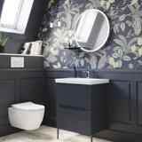 Badezimmer-Inspiration mit dunkelblauen Wandpaneelen, romantischer Blumen-Tapete, dunkelblauem Waschtischunterschrank mit weichen Formen und einem schönen runden Spiegel mit Beleuchtung, das ein Vintage-Flair verleiht