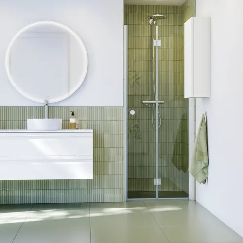 Badezimmerinspiration mit weißen Badmöbeln, elegantem Rundspiegel und Duschnische mit Falttür aus Klarglas und Profilen aus satinierten, grünen Langfliesen sorgen für einen edlen Look.