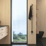 Stilvolles Badezimmer im skandinavischen und Japandi-Stil mit hellen Holzwänden, rundem Spiegel und minimalistischen Badezimmermöbeln.