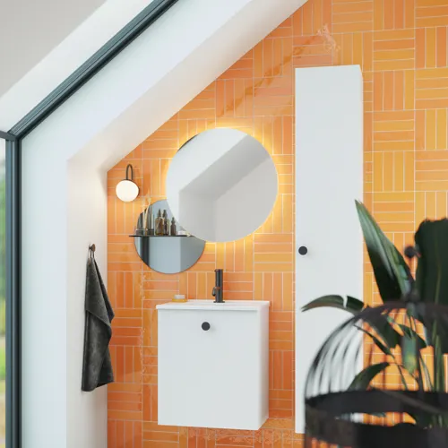 Badezimmer mit schräger Decke, inspiriert durch einen kleinen weißen Waschtisch und einen Hochschrank mit runden schwarzen Griffen, sowie einem schönen runden Spiegel, orangefarbene Fliesen geben einen frischen und modernen Look.