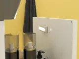 Kleine Badezimmerinspiration mit weißem Waschtisch mit schwarzem Griff und schwarzem elegantem Waschbecken, schönem rundem Spiegel mit schwarzem Rand, Terrazzo-Wand und -Boden und gelben Wänden für einen mutigen und modernen Look.